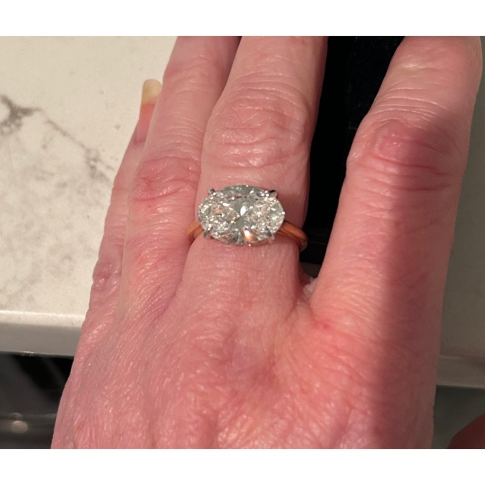 Oval lab grown 5.2 carat diamond set in rose gold band with diamond hidden halo.